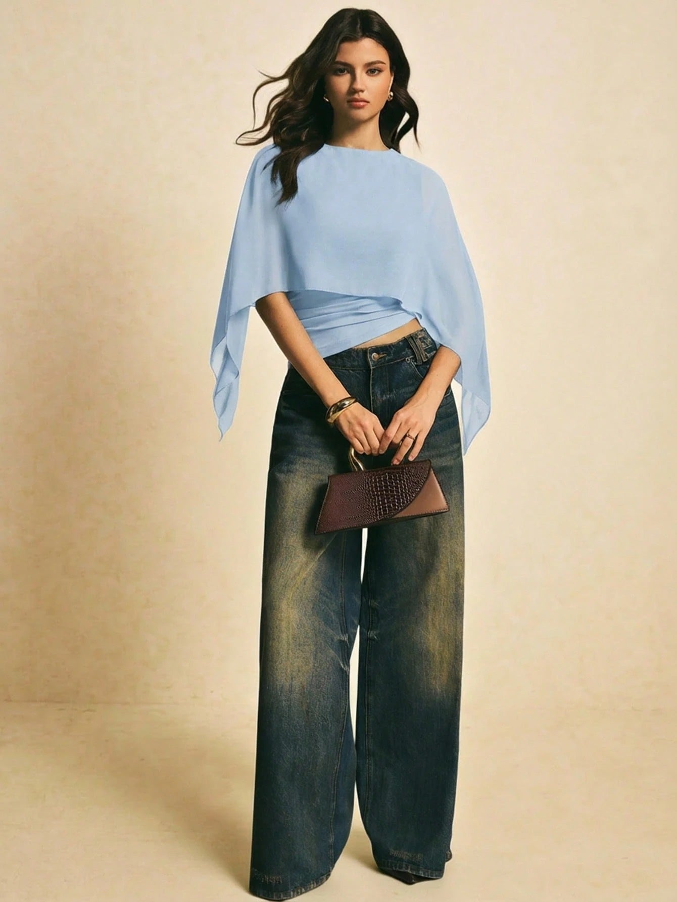 Woman wearing a light blue solid color elegant shawl blouse with cape sleeves paired with dark denim jeans