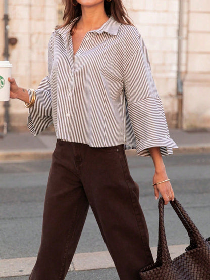 Woman wearing a light khaki vertical striped drop-shoulder button-down shirt paired with brown pants, holding a dark woven handbag