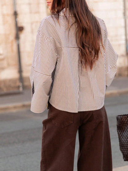 Woman wearing a light khaki vertical striped drop-shoulder button-down shirt paired with brown pants, holding a dark woven handbag