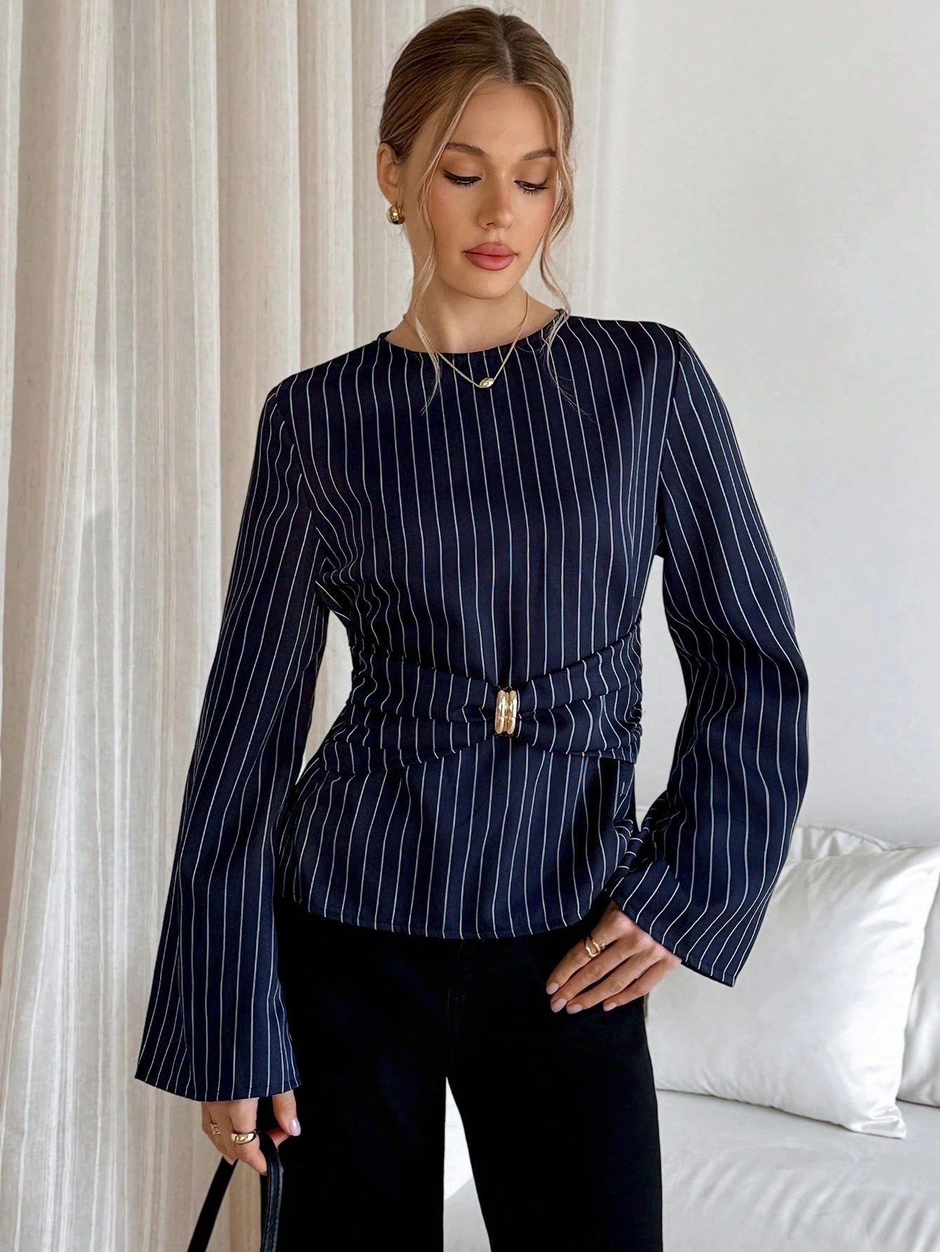 Woman wearing a navy blue pinstripe long sleeve blouse featuring a metal ring decor waist detail and dark trousers