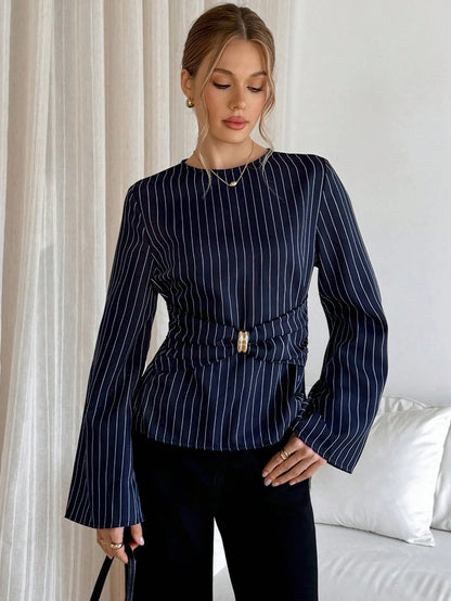 Woman wearing a navy blue pinstripe long sleeve blouse featuring a metal ring decor waist detail and dark trousers