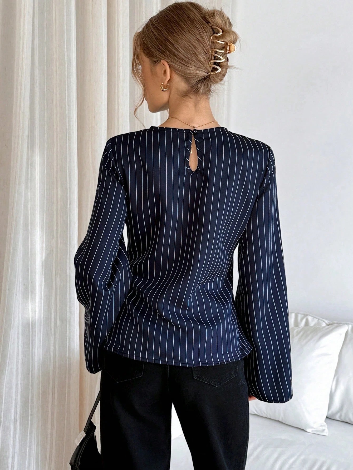 Woman wearing a navy blue pinstripe long sleeve blouse featuring a metal ring decor waist detail and dark trousers