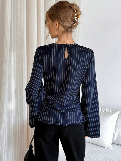 Woman wearing a navy blue pinstripe long sleeve blouse featuring a metal ring decor waist detail and dark trousers