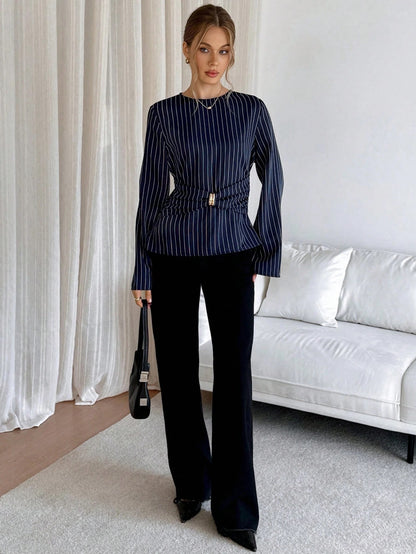 Woman wearing a navy blue pinstripe long sleeve blouse featuring a metal ring decor waist detail and dark trousers