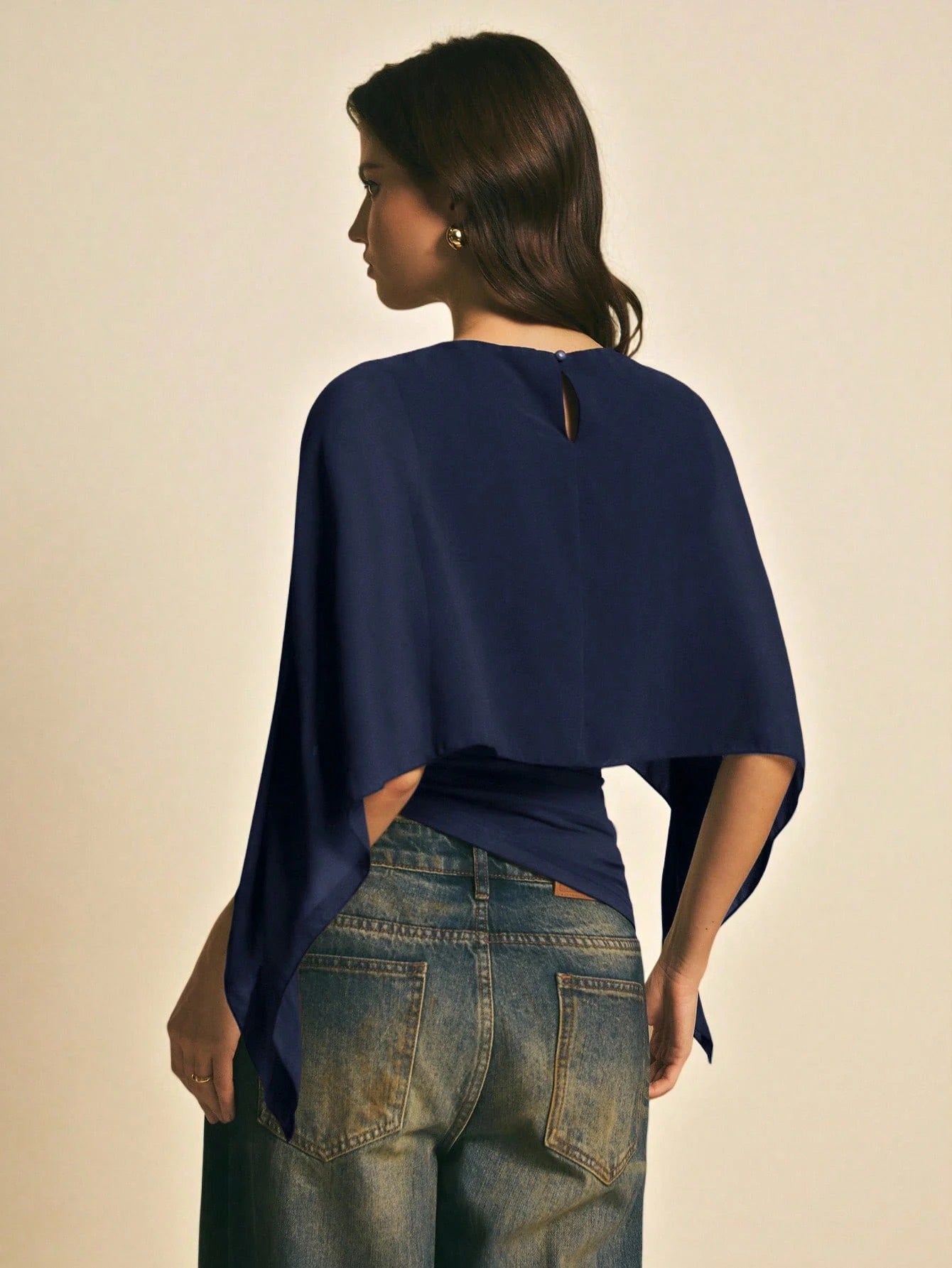 Woman wearing a navy blue solid color elegant shawl blouse with cape sleeves paired with dark denim jeans