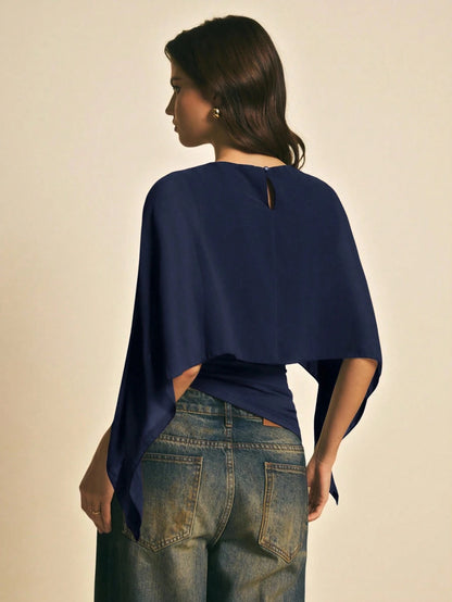 Woman wearing a navy blue solid color elegant shawl blouse with cape sleeves paired with dark denim jeans