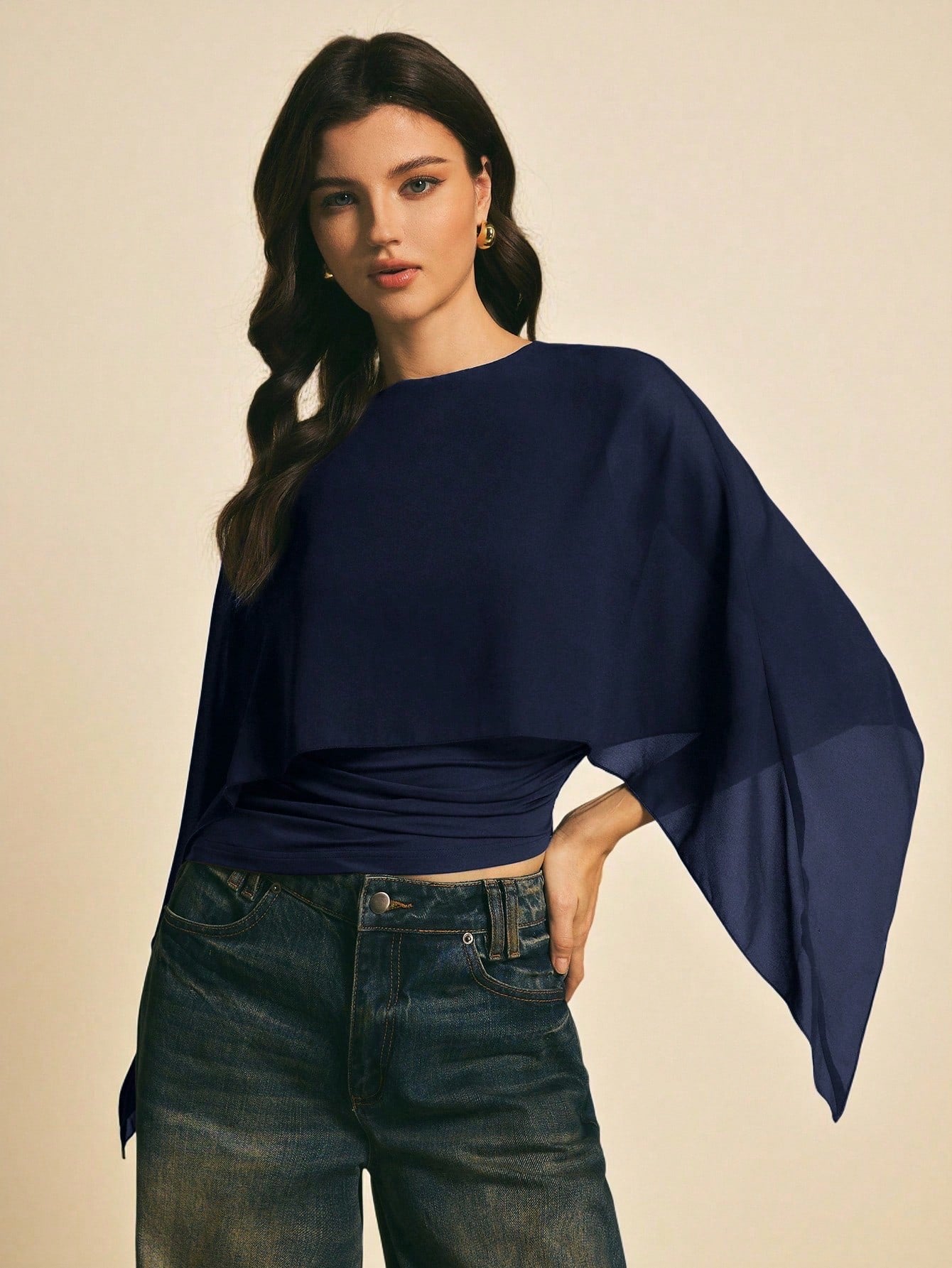 Woman wearing a navy blue solid color elegant shawl blouse with cape sleeves paired with dark denim jeans