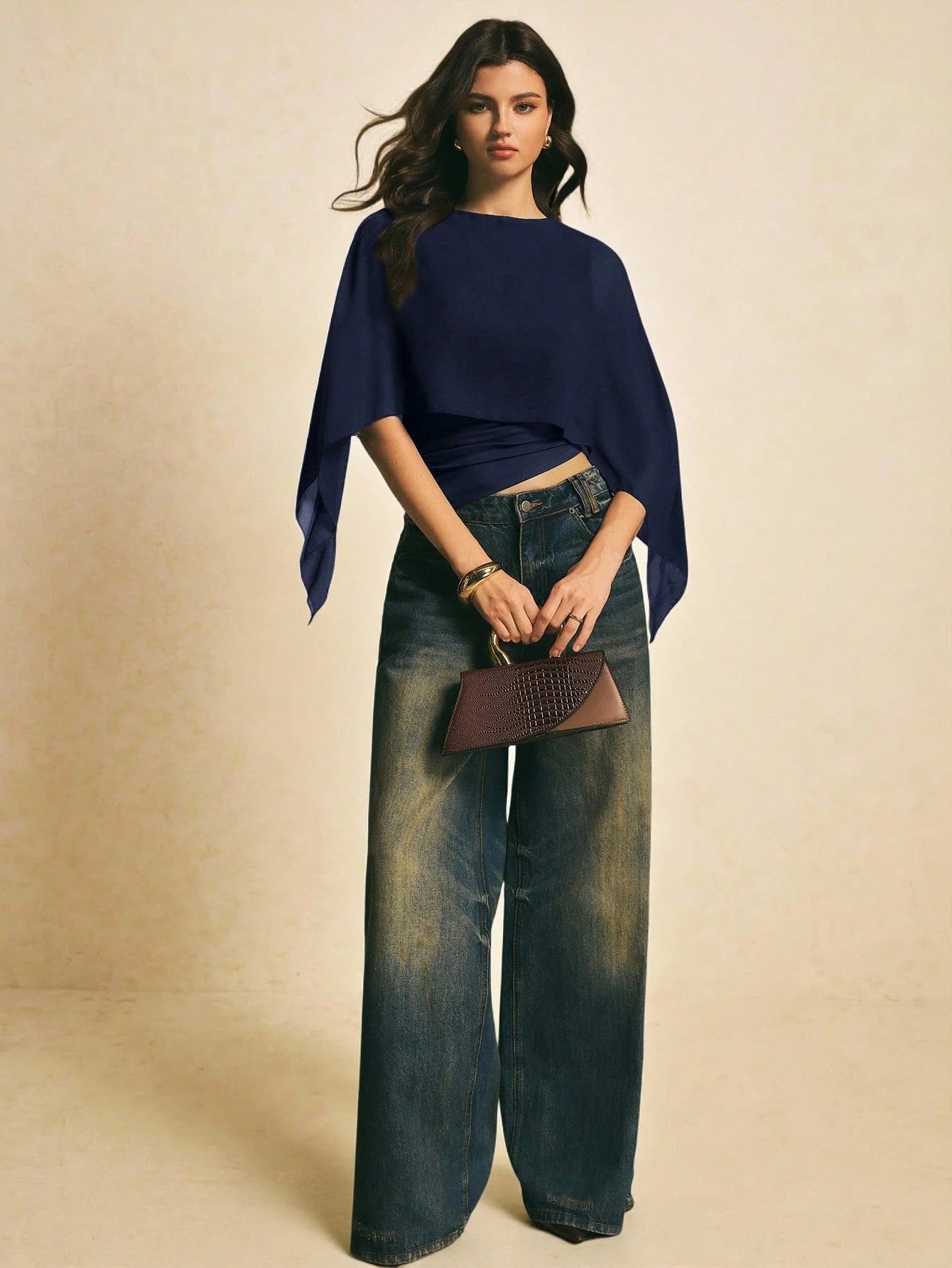 Woman wearing a navy blue solid color elegant shawl blouse with cape sleeves paired with dark denim jeans