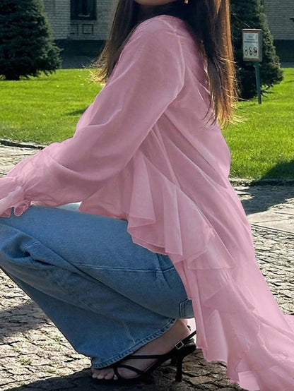 Woman wearing a pink long-sleeve V-neck top with an asymmetrical cascading ruffle high-low hem paired with blue jeans and holding a gold clutch.