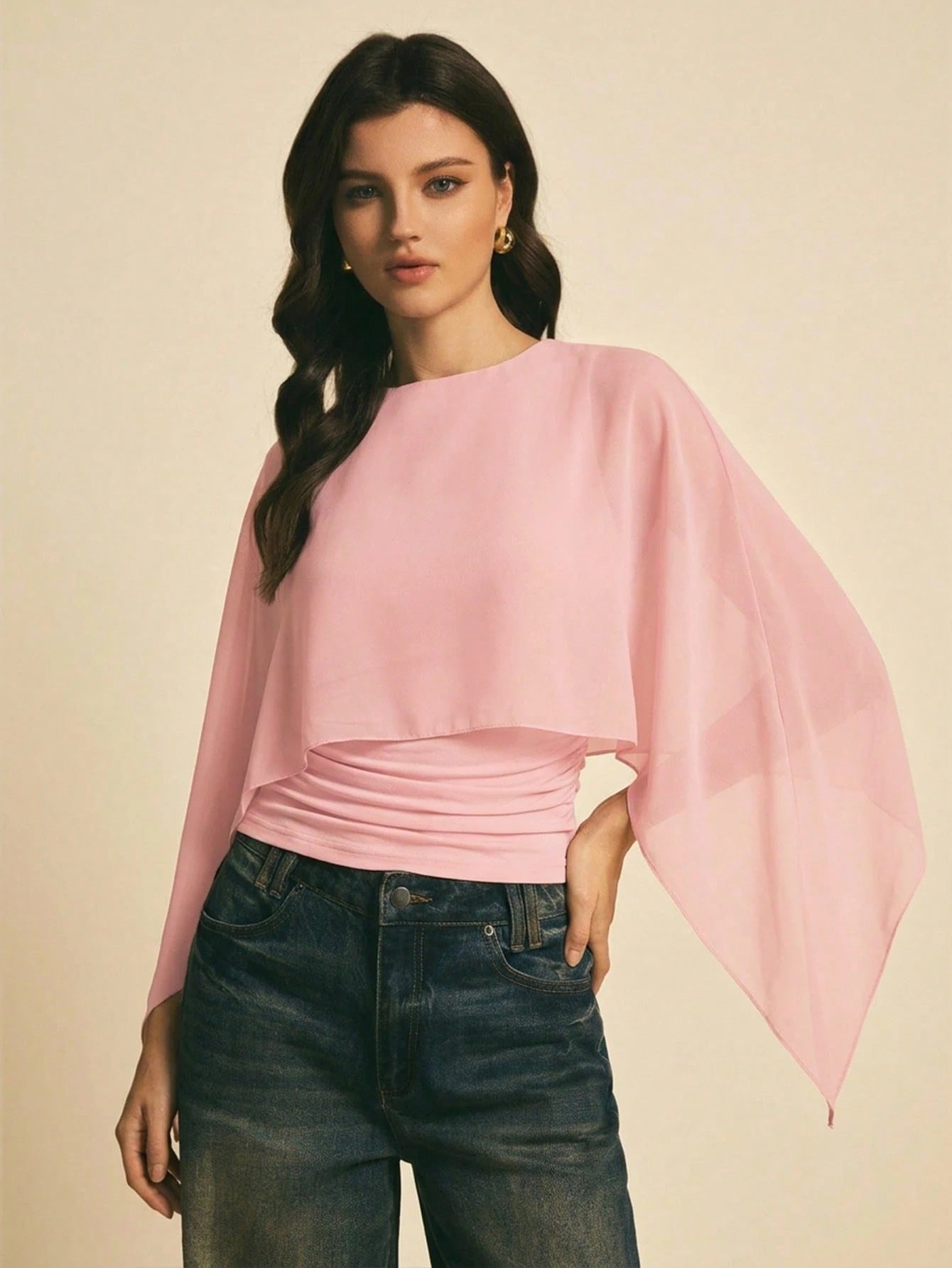 Woman wearing a pink solid color elegant shawl blouse with cape sleeves paired with dark denim jeans