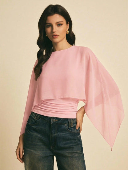 Woman wearing a pink solid color elegant shawl blouse with cape sleeves paired with dark denim jeans