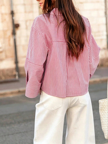 Woman wearing a red vertical striped drop-shoulder button-down shirt paired with white pants, holding a dark woven handbag