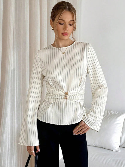 Woman wearing a white pinstripe long sleeve blouse featuring a metal ring decor waist detail and dark trousers