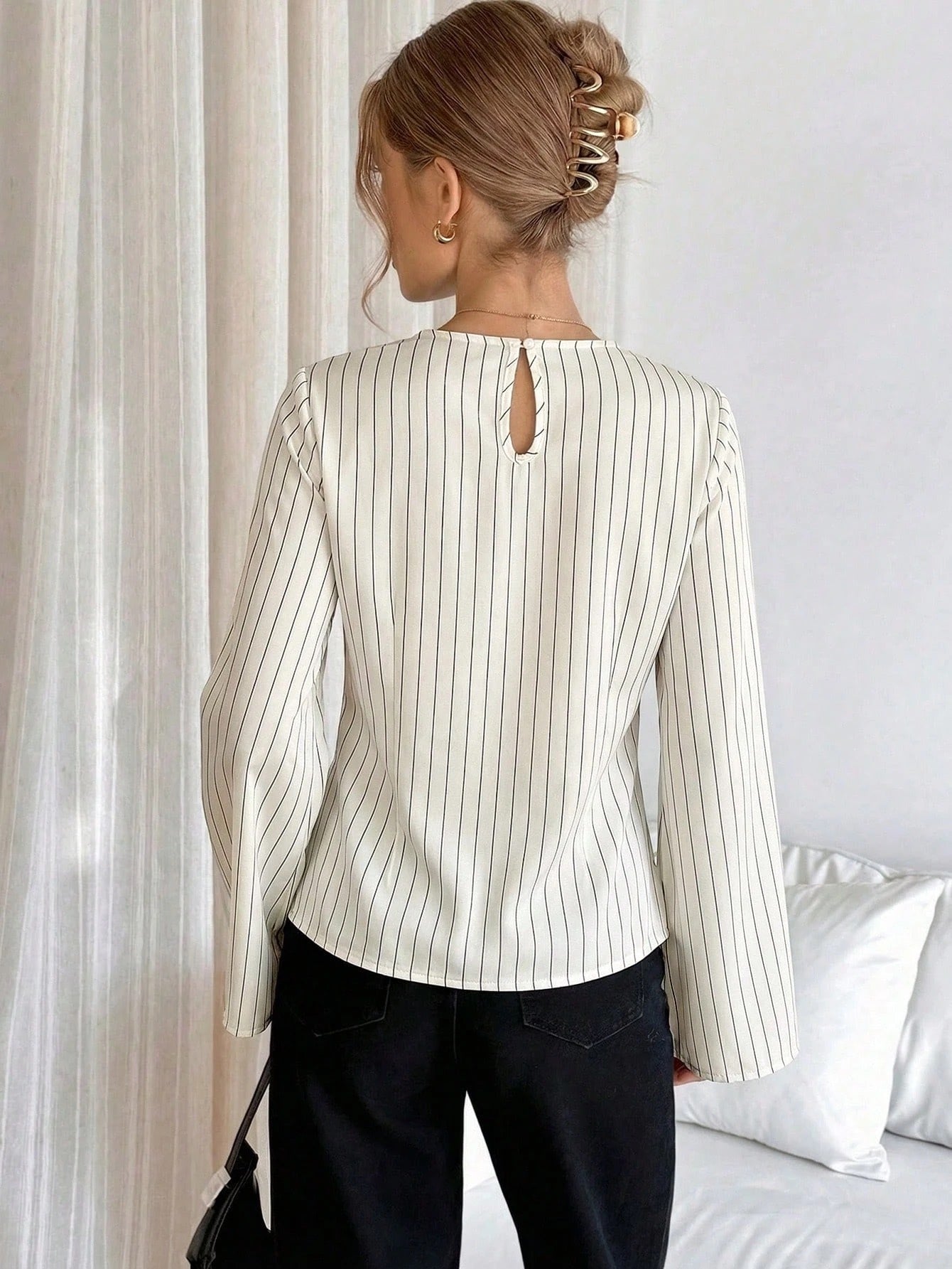 Woman wearing a white pinstripe long sleeve blouse featuring a metal ring decor waist detail and dark trousers