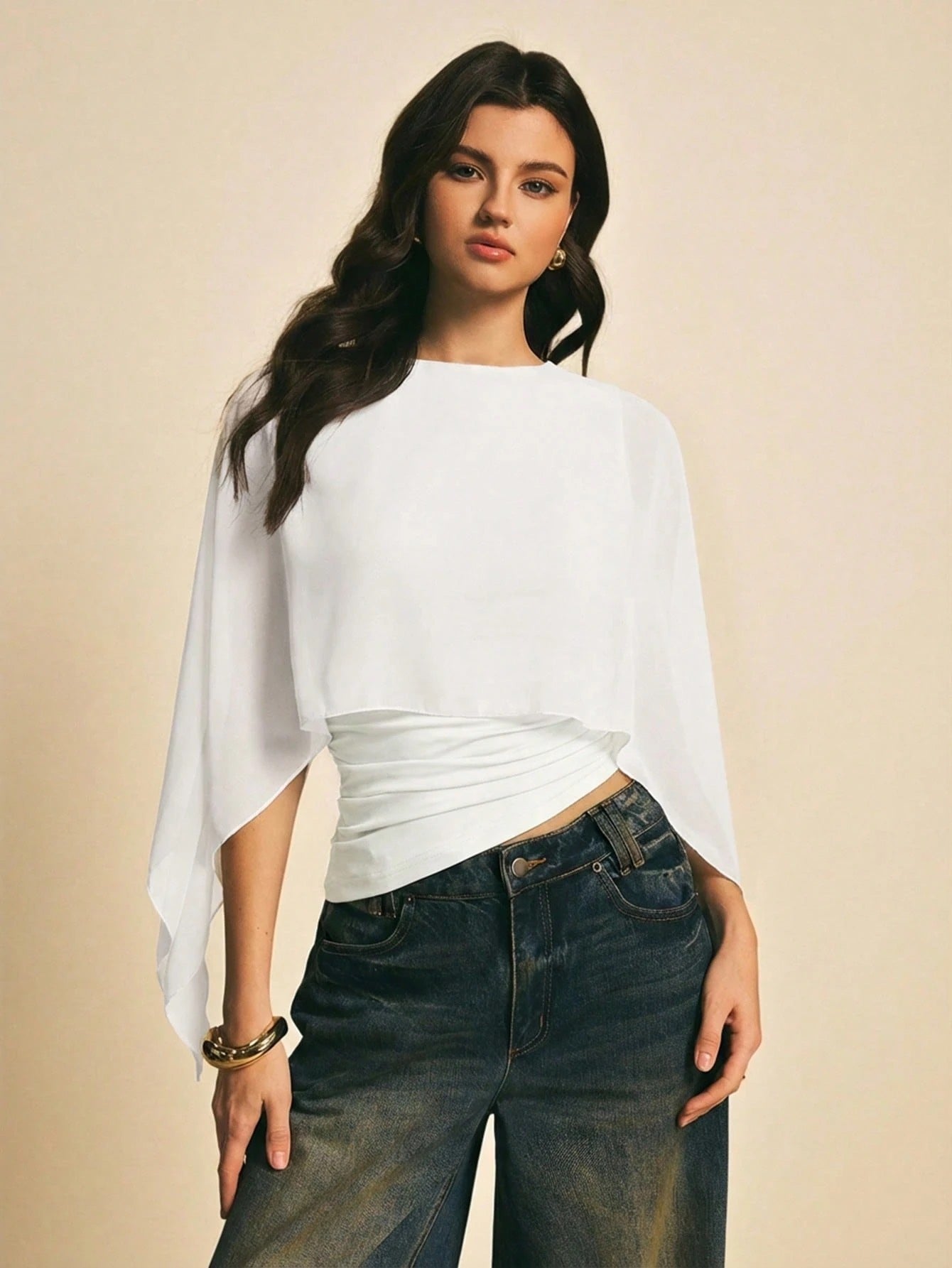 Woman wearing a white solid color elegant shawl blouse with cape sleeves paired with dark denim jeans