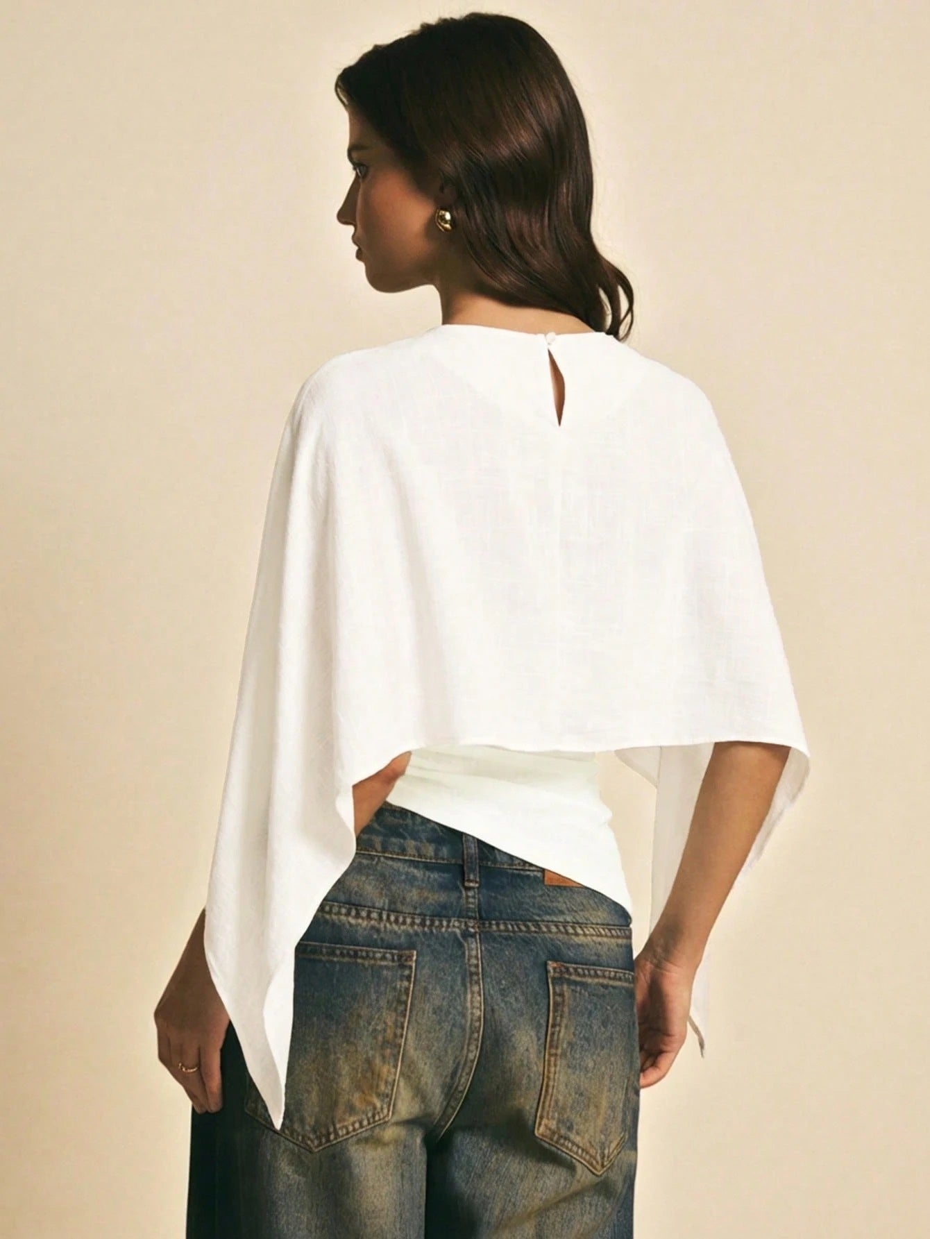 Woman wearing a white solid color elegant shawl blouse with cape sleeves paired with dark denim jeans
