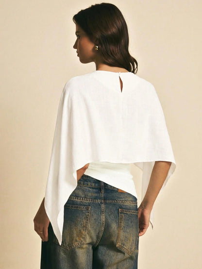 Woman wearing a white solid color elegant shawl blouse with cape sleeves paired with dark denim jeans