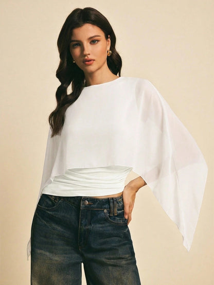 Woman wearing a white solid color elegant shawl blouse with cape sleeves paired with dark denim jeans