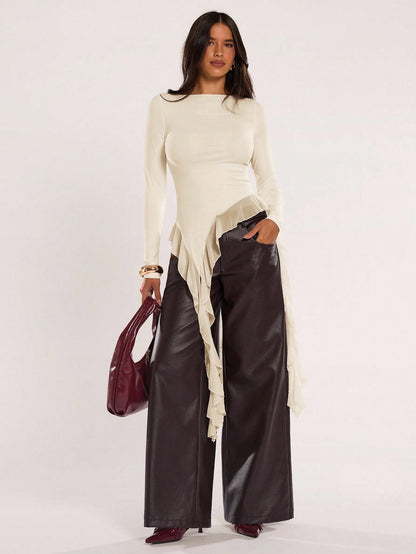 Woman wearing an apricot fitted long sleeve top with an asymmetric ruffle hem paired with dark brown faux leather pants
