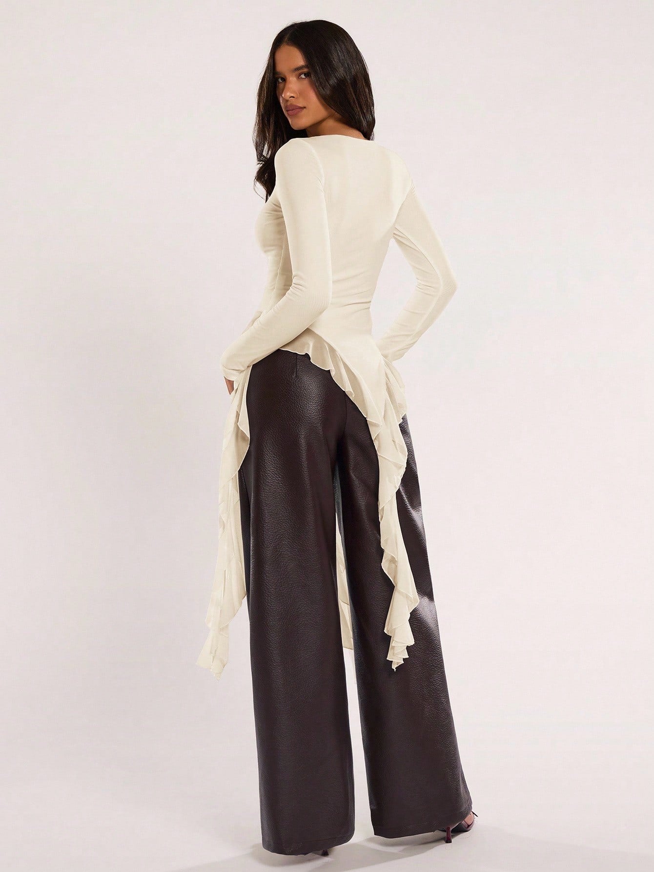 Woman wearing an apricot fitted long sleeve top with an asymmetric ruffle hem paired with dark brown faux leather pants
