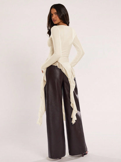 Woman wearing an apricot fitted long sleeve top with an asymmetric ruffle hem paired with dark brown faux leather pants