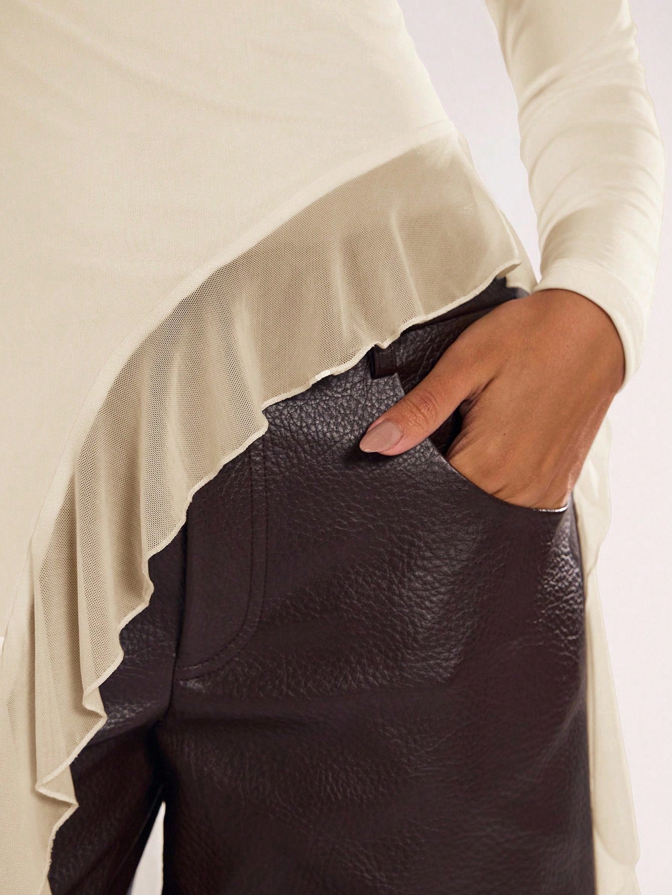 Woman wearing an apricot fitted long sleeve top with an asymmetric ruffle hem paired with dark brown faux leather pants