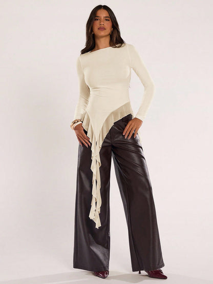 Woman wearing an apricot fitted long sleeve top with an asymmetric ruffle hem paired with dark brown faux leather pants