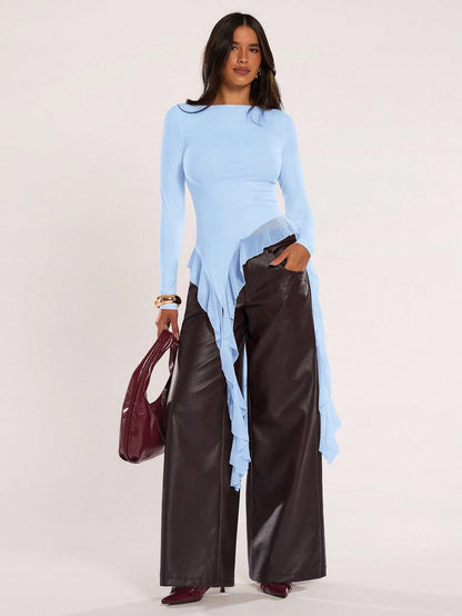 Woman wearing an baby blue fitted long sleeve top with an asymmetric ruffle hem paired with dark brown faux leather pants