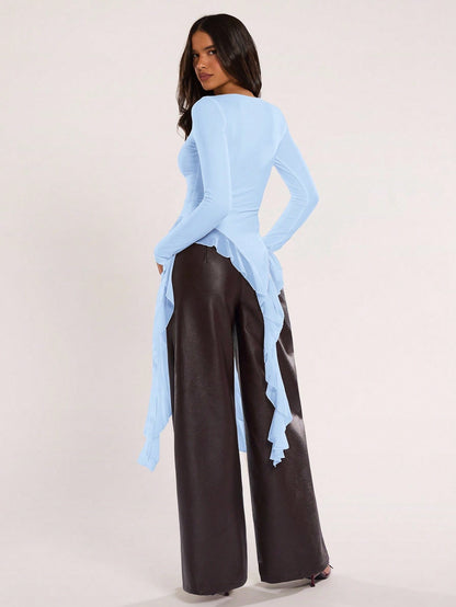 Woman wearing an baby blue fitted long sleeve top with an asymmetric ruffle hem paired with dark brown faux leather pants