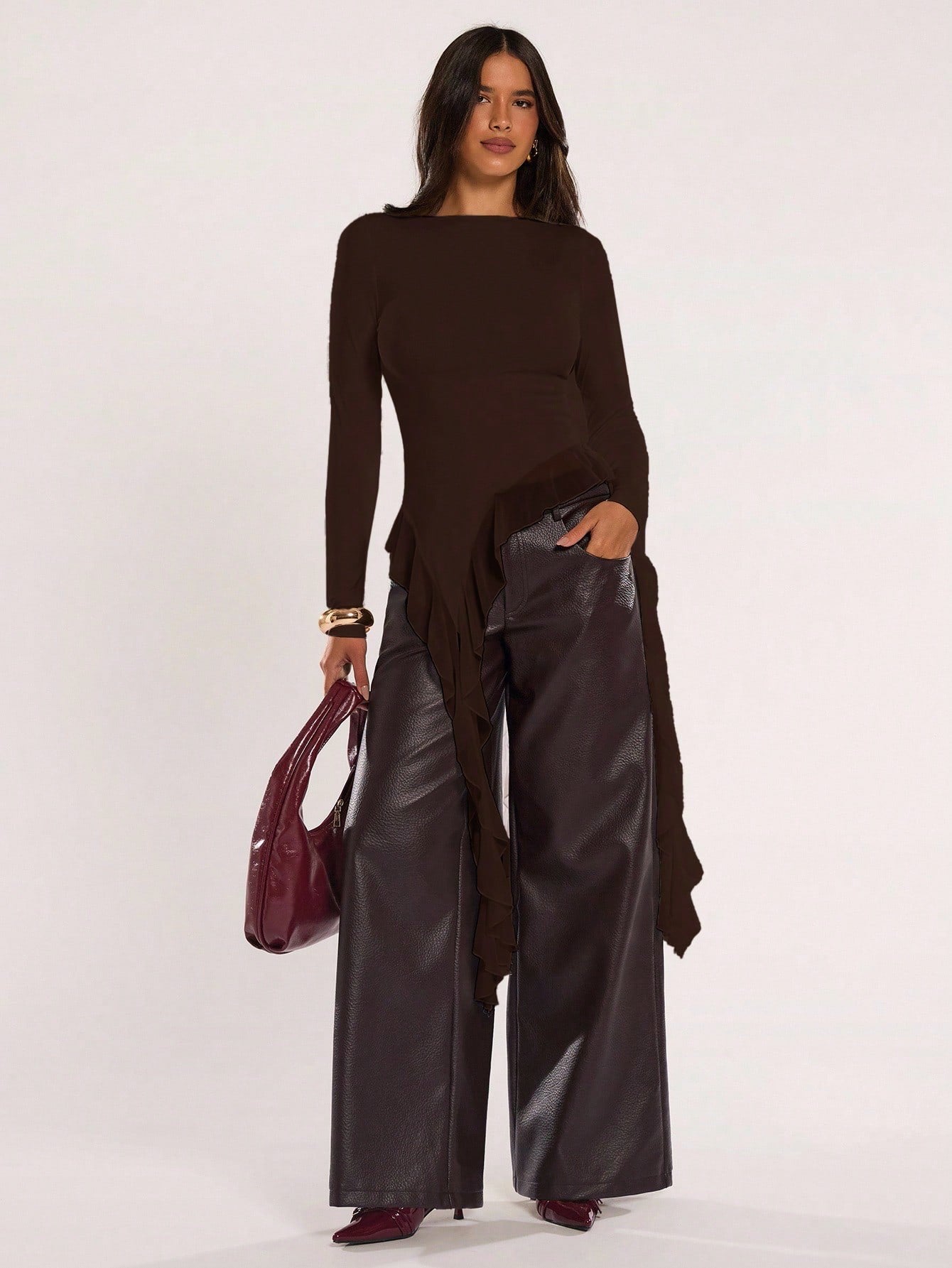 Woman wearing an coffee brown fitted long sleeve top with an asymmetric ruffle hem paired with dark brown faux leather pants