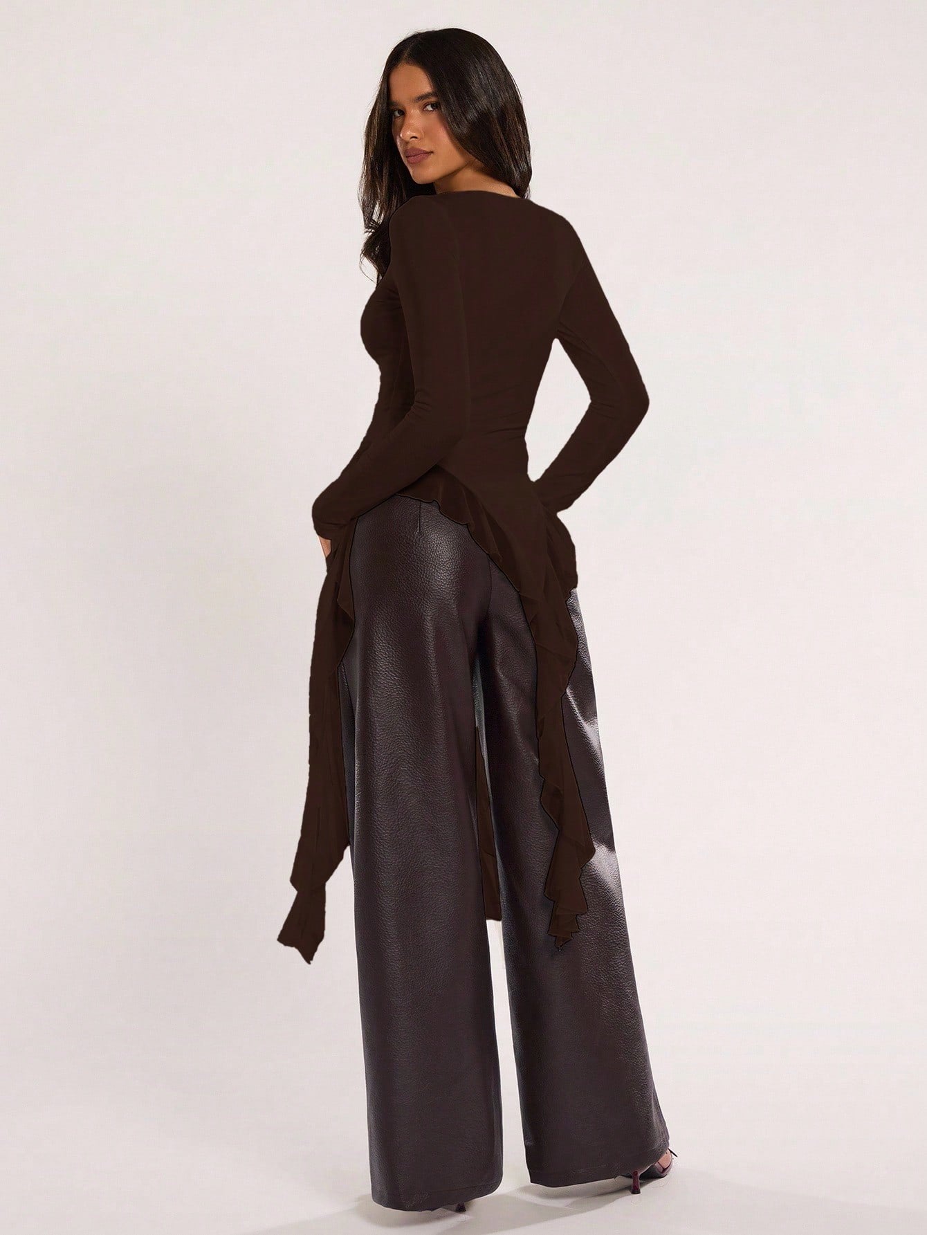 Woman wearing an coffee brown fitted long sleeve top with an asymmetric ruffle hem paired with dark brown faux leather pants