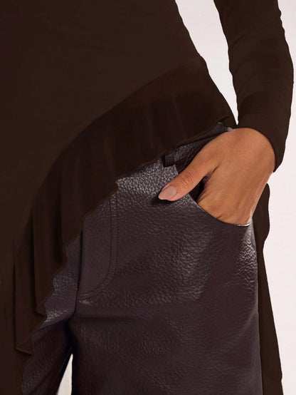 Woman wearing an coffee brown fitted long sleeve top with an asymmetric ruffle hem paired with dark brown faux leather pants