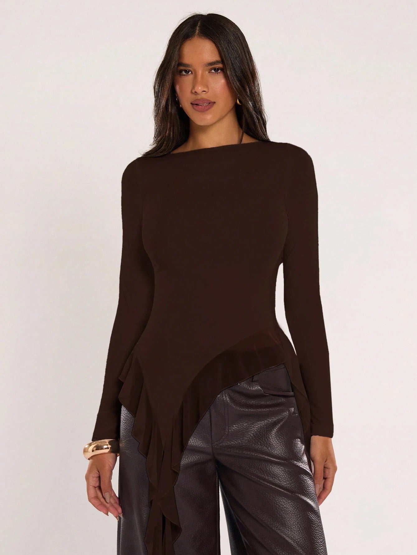 Woman wearing an coffee brown fitted long sleeve top with an asymmetric ruffle hem paired with dark brown faux leather pants