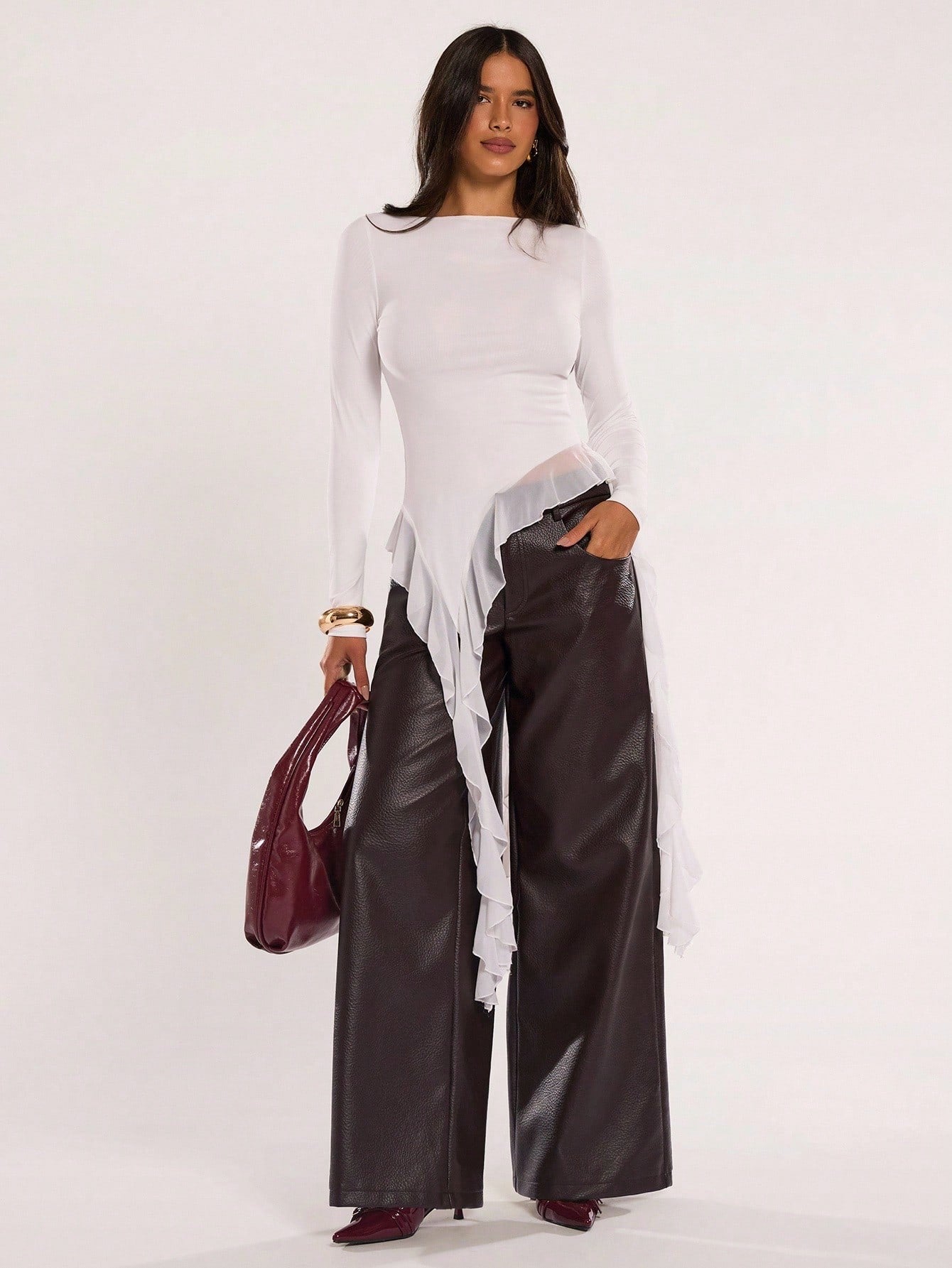 Woman wearing an off-white fitted long sleeve top with an asymmetric ruffle hem paired with dark brown faux leather pants
