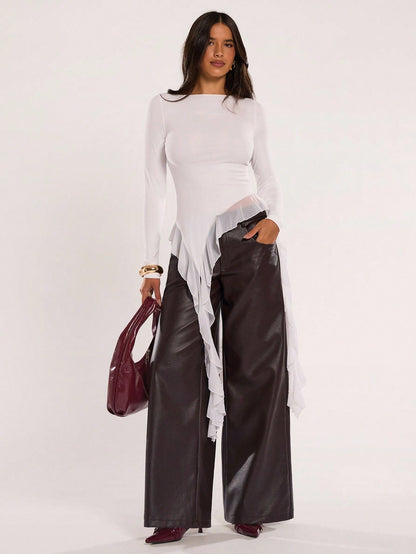 Woman wearing an off-white fitted long sleeve top with an asymmetric ruffle hem paired with dark brown faux leather pants