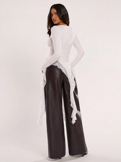 Woman wearing an off-white fitted long sleeve top with an asymmetric ruffle hem paired with dark brown faux leather pants