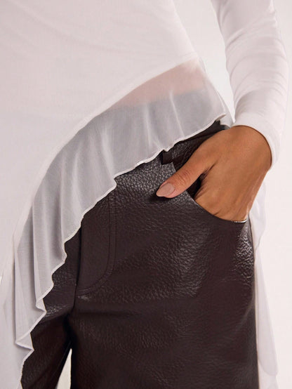 Woman wearing an off-white fitted long sleeve top with an asymmetric ruffle hem paired with dark brown faux leather pants
