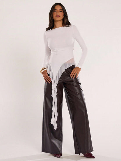 Woman wearing an off-white fitted long sleeve top with an asymmetric ruffle hem paired with dark brown faux leather pants