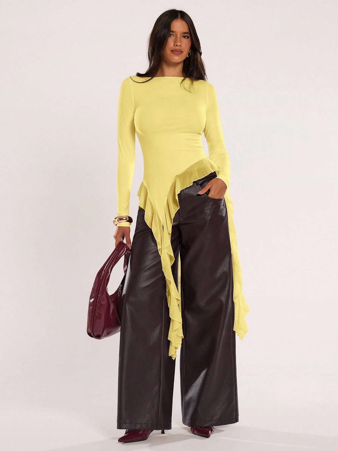 Woman wearing an yellow fitted long sleeve top with an asymmetric ruffle hem paired with dark brown faux leather pants