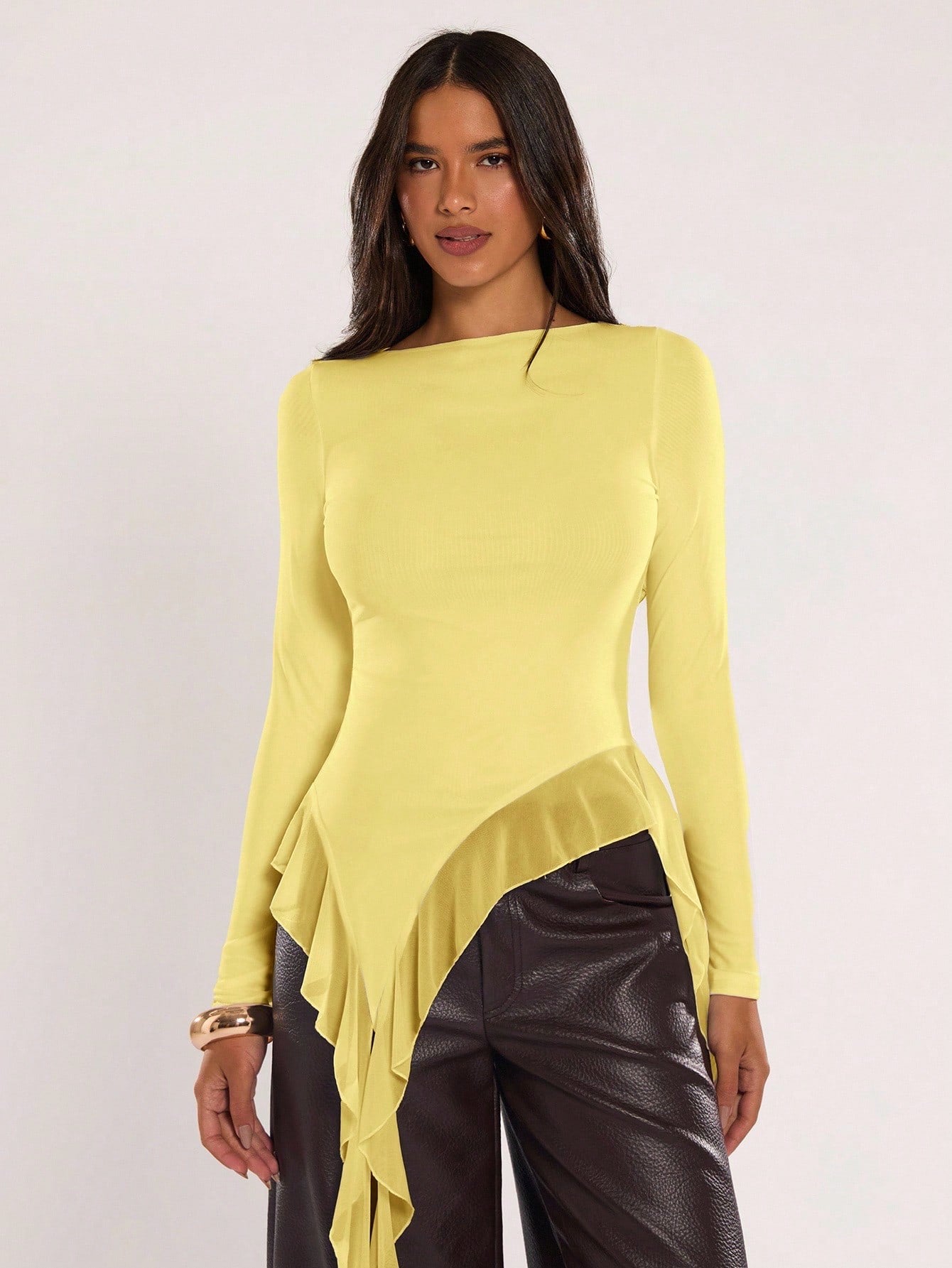 Woman wearing an yellow fitted long sleeve top with an asymmetric ruffle hem paired with dark brown faux leather pants