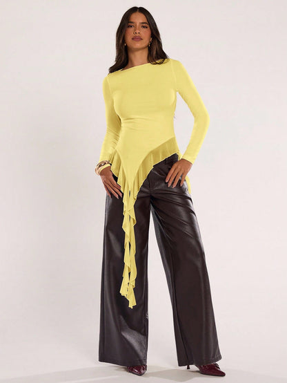 Woman wearing an yellow fitted long sleeve top with an asymmetric ruffle hem paired with dark brown faux leather pants