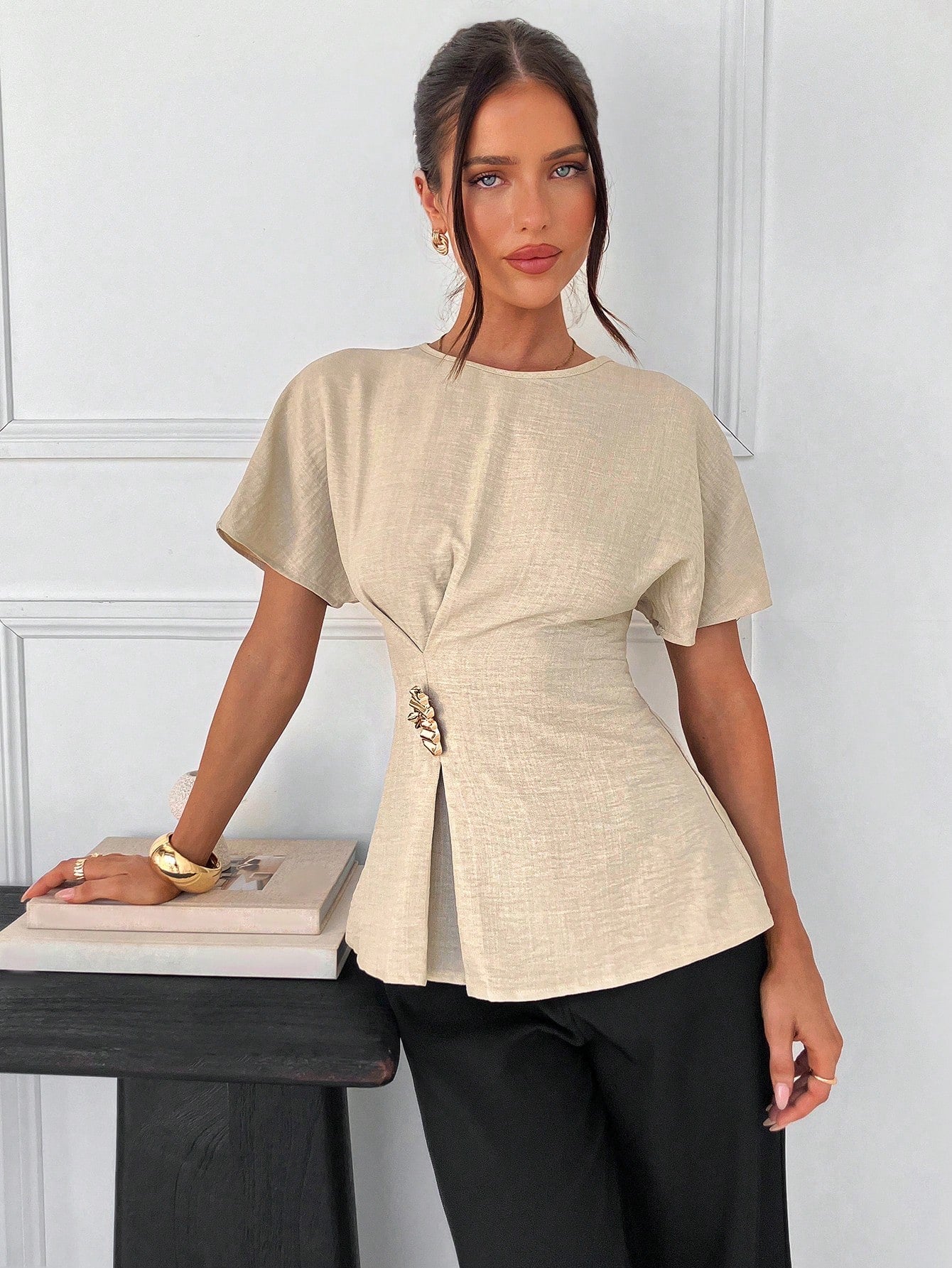 Women's apricot short-sleeve round neck blouse with a statement gold side waist buckle paired with black trousers for an office look.