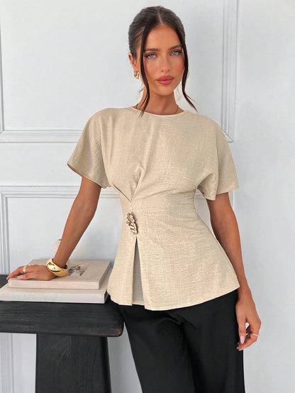 Women's apricot short-sleeve round neck blouse with a statement gold side waist buckle paired with black trousers for an office look.