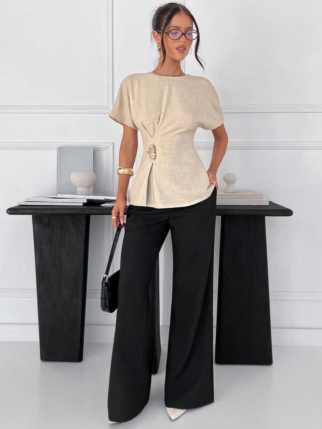Women's apricot short-sleeve round neck blouse with a statement gold side waist buckle paired with black trousers for an office look.