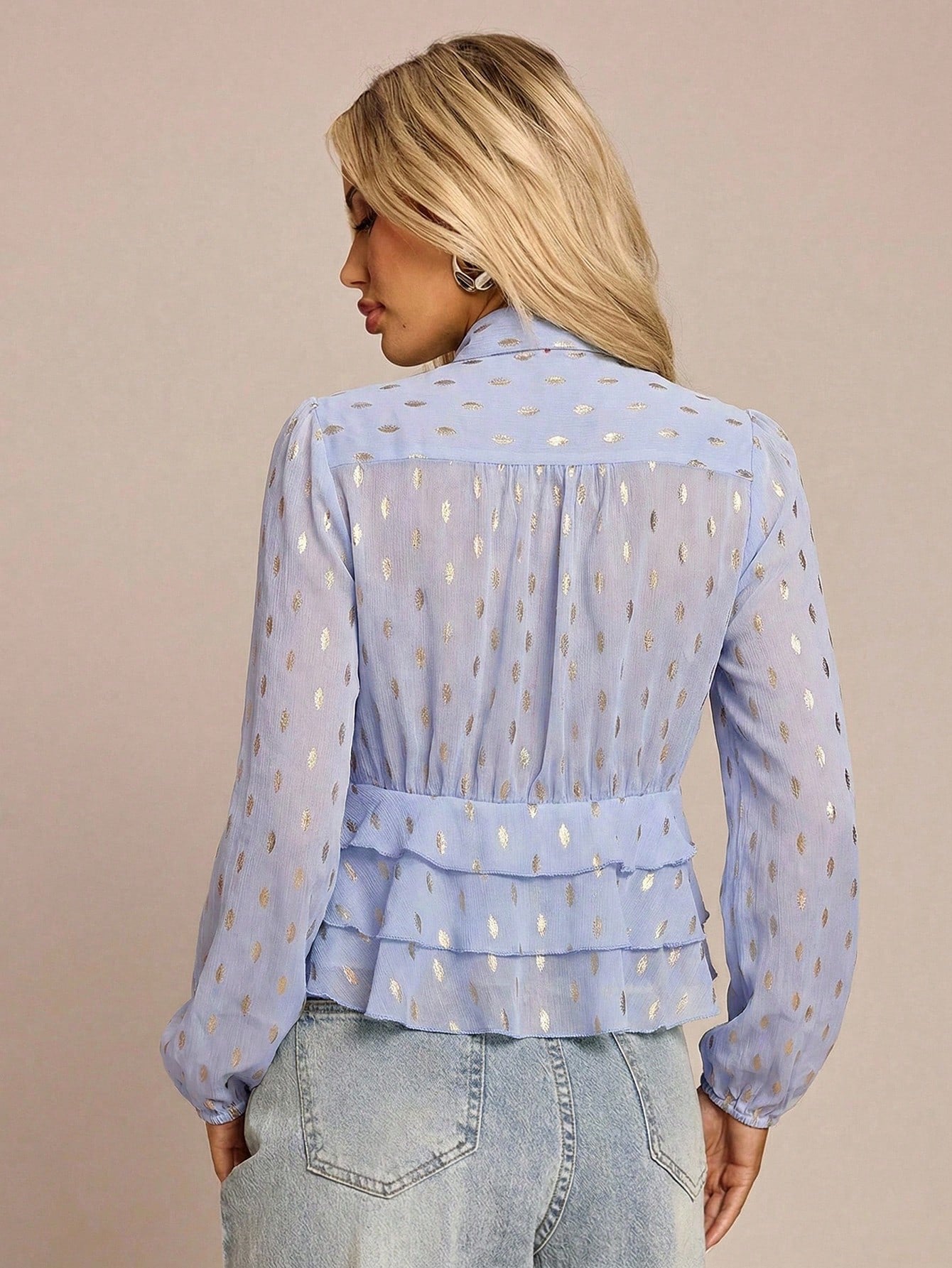 Women's baby blue long-sleeve chiffon blouse with metallic foil dots, a V-neck, a scarf tie, and a tiered ruffled hem paired with blue jeans.
