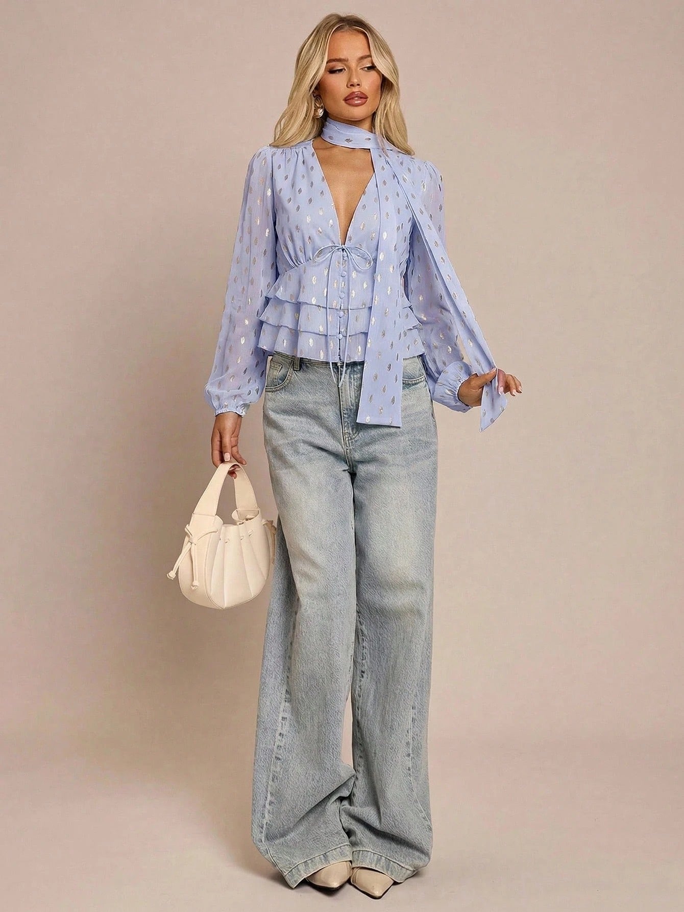 Women's baby blue long-sleeve chiffon blouse with metallic foil dots, a V-neck, a scarf tie, and a tiered ruffled hem paired with blue jeans.