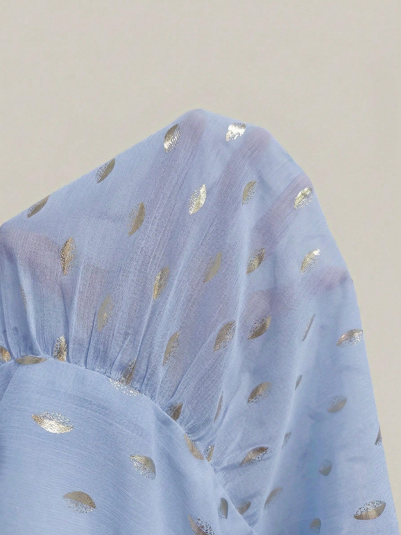 Women's baby blue long-sleeve chiffon blouse with metallic foil dots, a V-neck, a scarf tie, and a tiered ruffled hem paired with blue jeans.