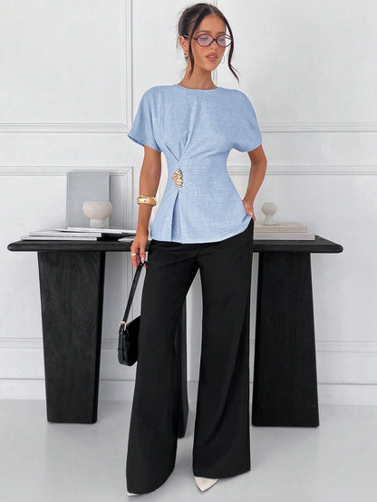 Women's baby blue short-sleeve round neck blouse with a statement gold side waist buckle paired with black trousers for an office look.