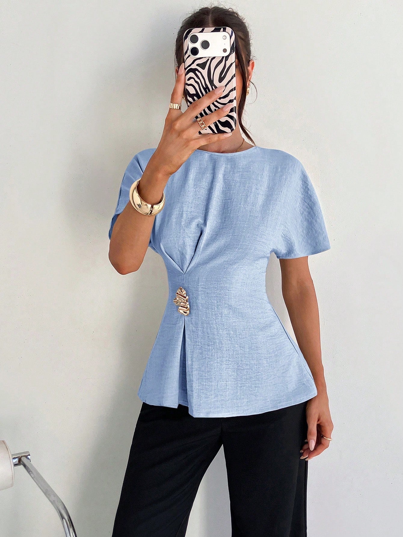 Women's baby blue short-sleeve round neck blouse with a statement gold side waist buckle paired with black trousers for an office look.