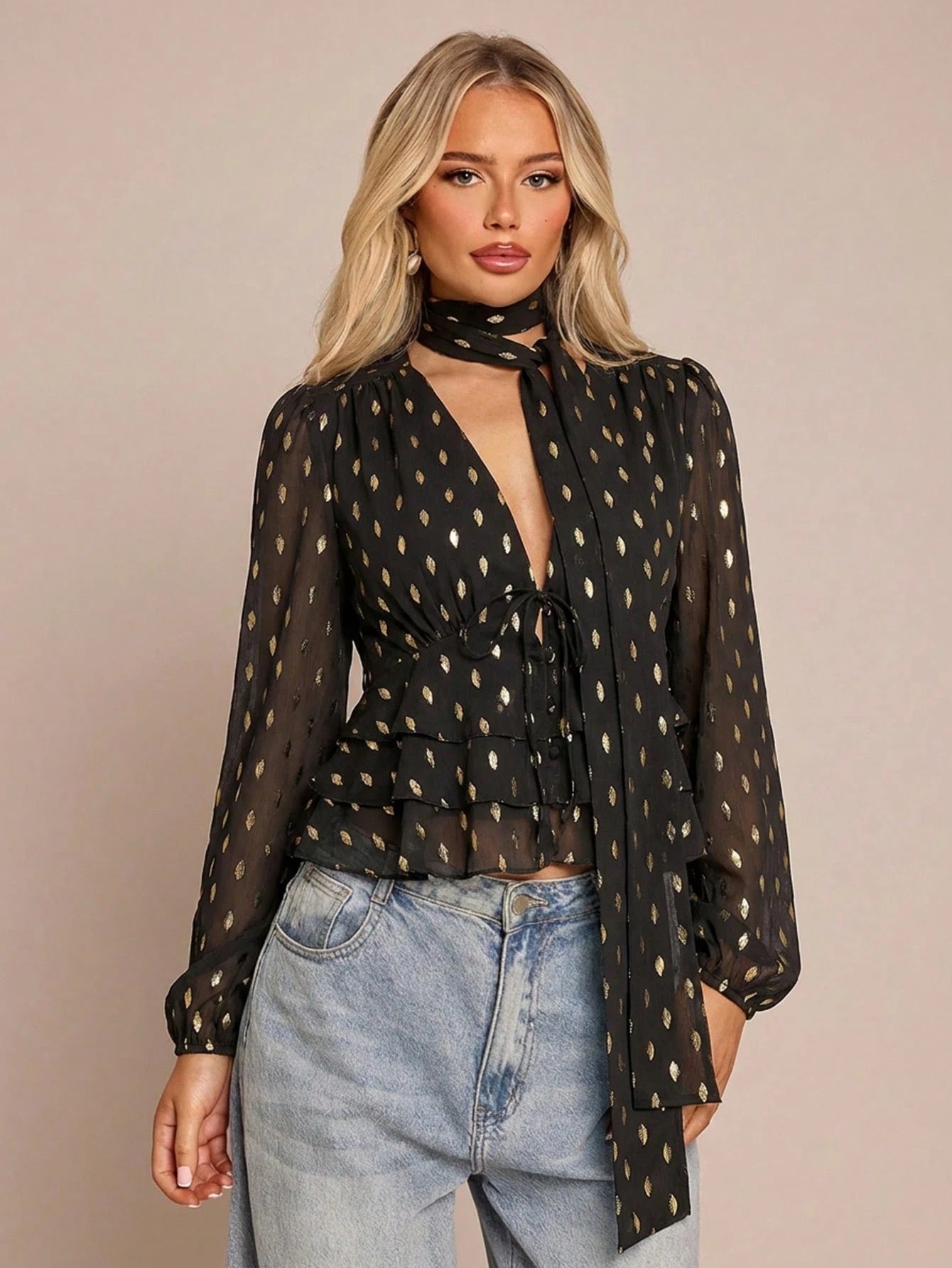 Women's black long-sleeve chiffon blouse with metallic foil dots, a V-neck, a scarf tie, and a tiered ruffled hem paired with blue jeans.